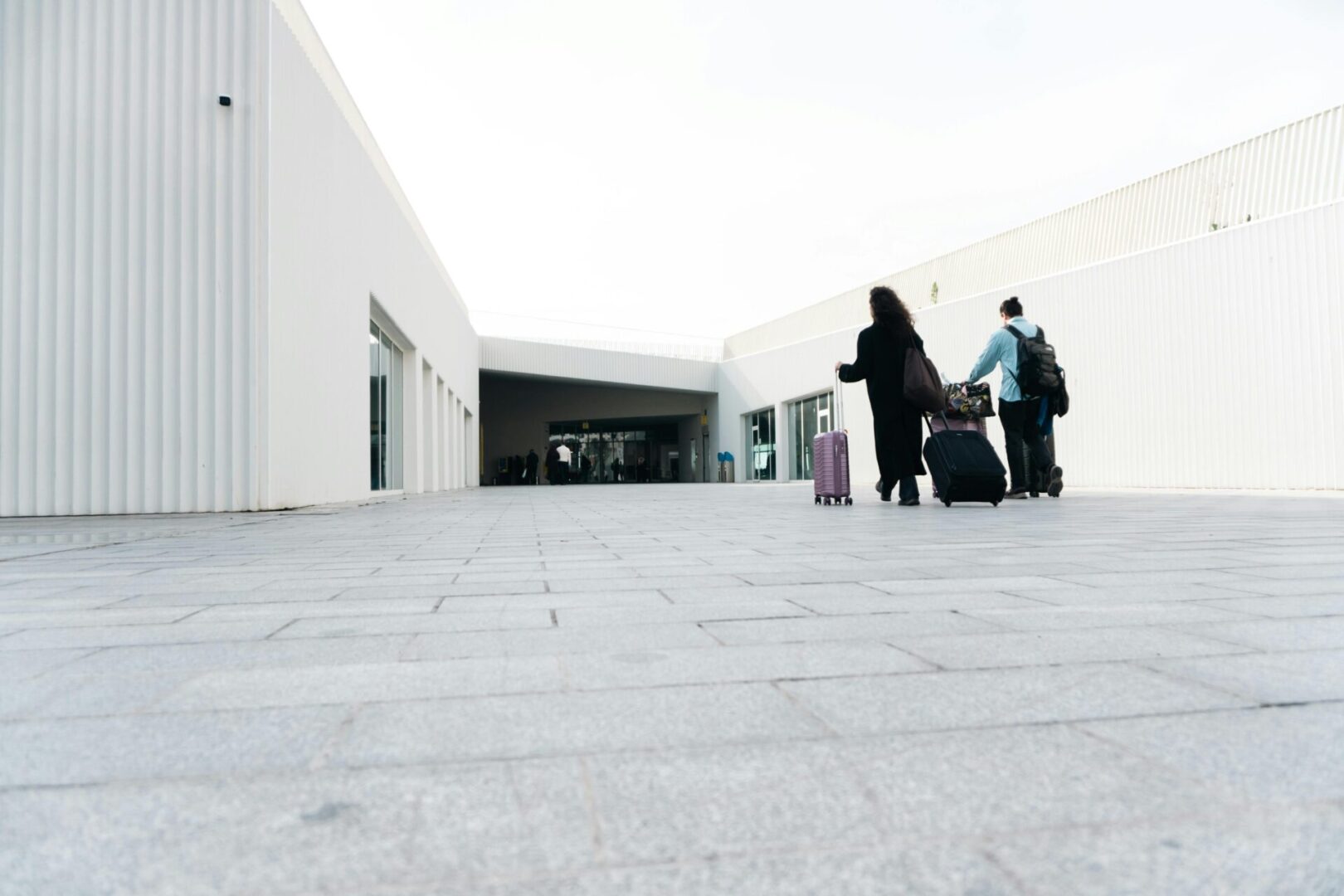 Travelers with luggage walk along a modern, open-air walkway.
