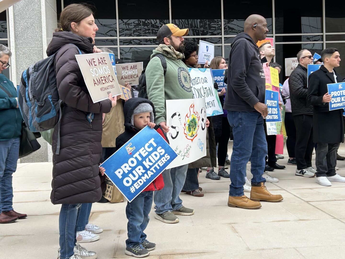 A group of people stand holding signs advocating for climate action and protecting education.