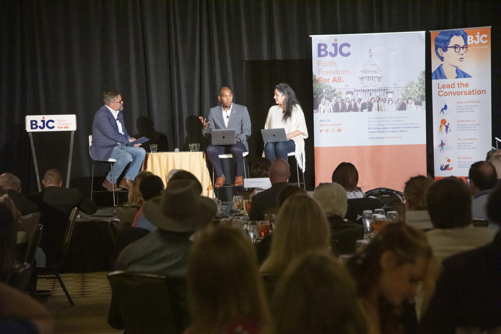 A panel discussion is taking place on a stage with an audience in attendance.