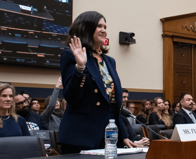 A person is raising their right hand in what appears to be a formal setting, possibly a hearing or courtroom.