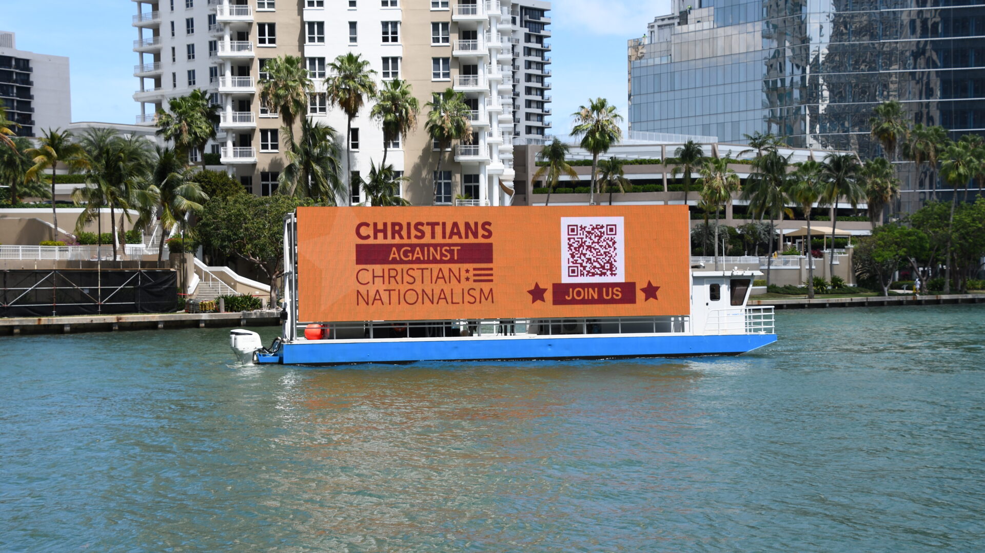 A large floating billboard with a QR code advertises a message for Christians on a body of water.