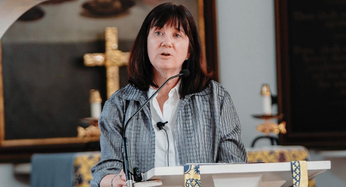 A person is speaking at a podium with a cross and candles in the background.