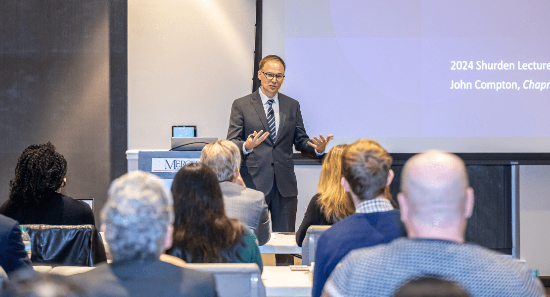 A person in a suit is giving a presentation to an attentive audience in a conference room.