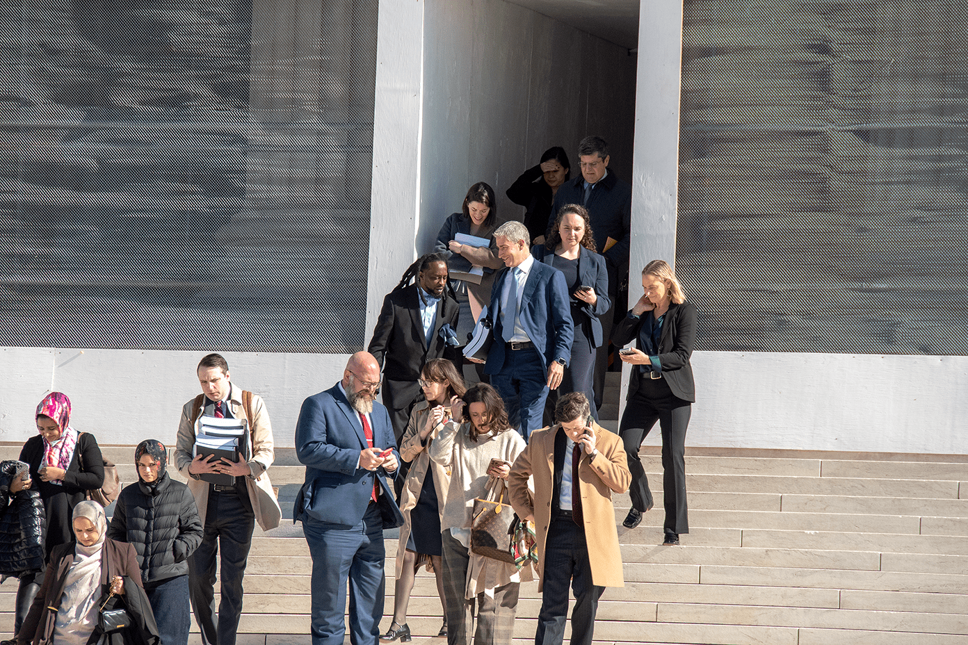 A group of professionally dressed individuals descends steps while engaged in conversation and checking their phones.