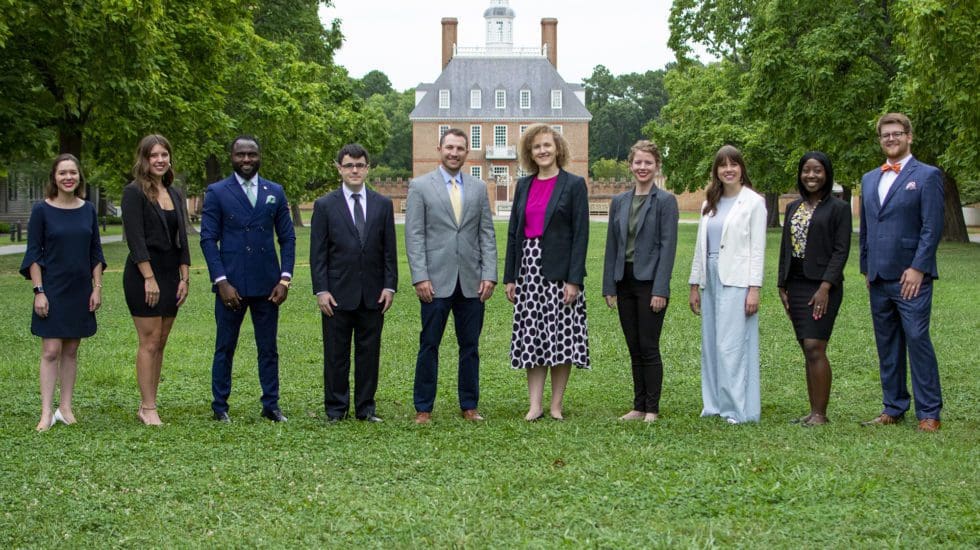 A group of people dressed formally stands on a grassy area with a historic building in the background.