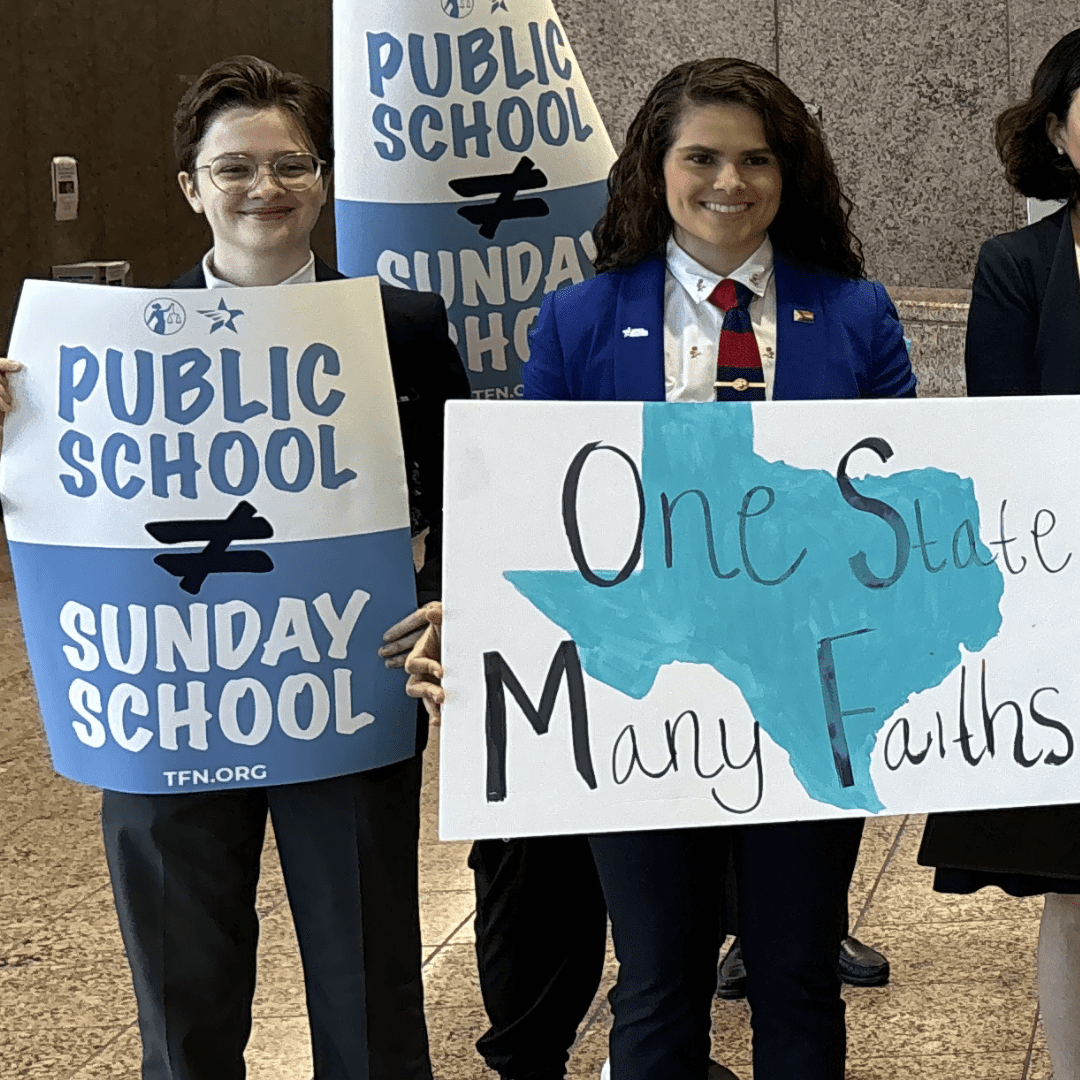 People are holding signs advocating for the separation of public school and religious instruction, with one highlighting "One State Many Faiths" alongside an image of Texas.