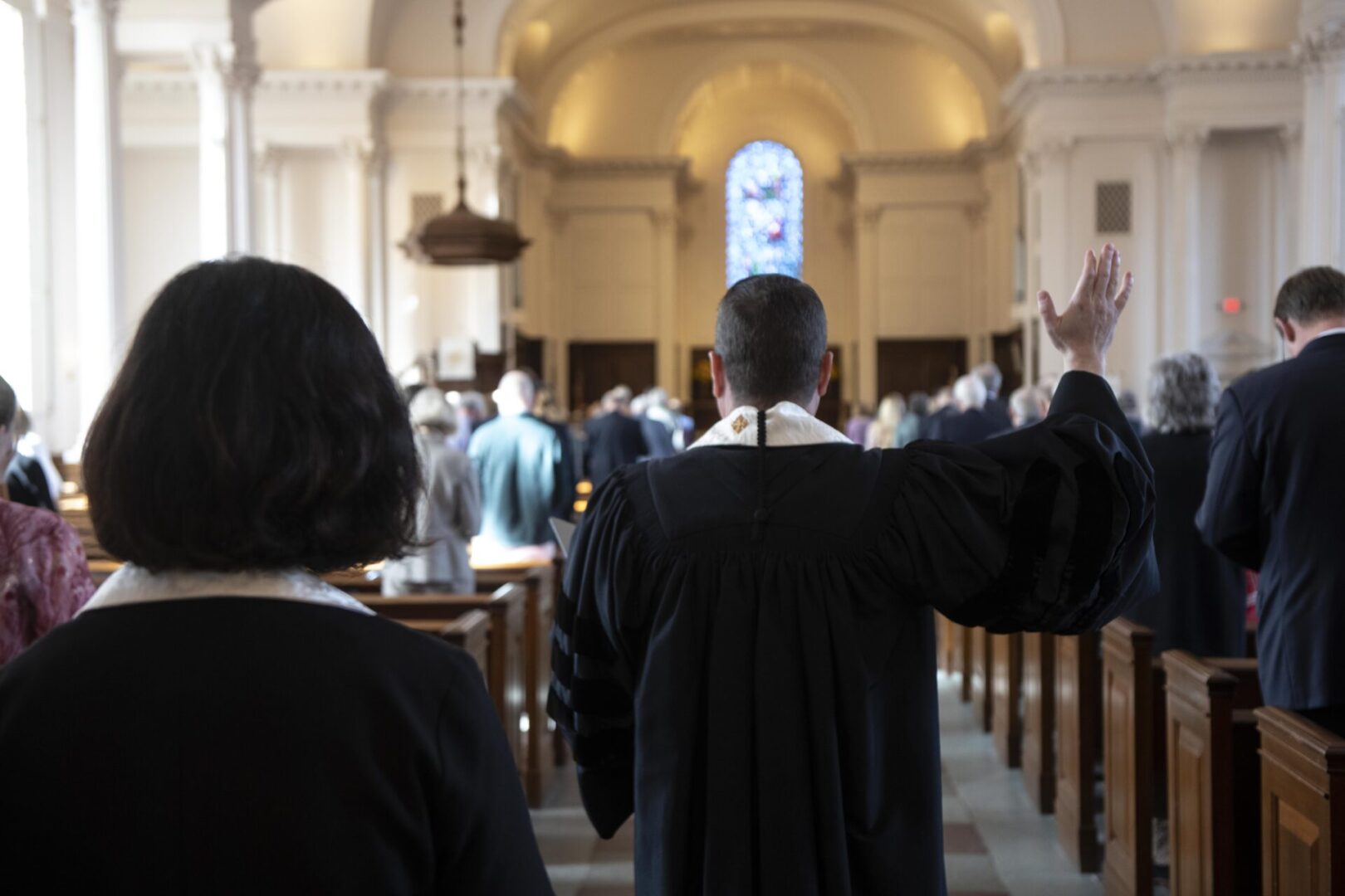 A religious service is taking place in a church with a person in robes gesturing towards the congregation.