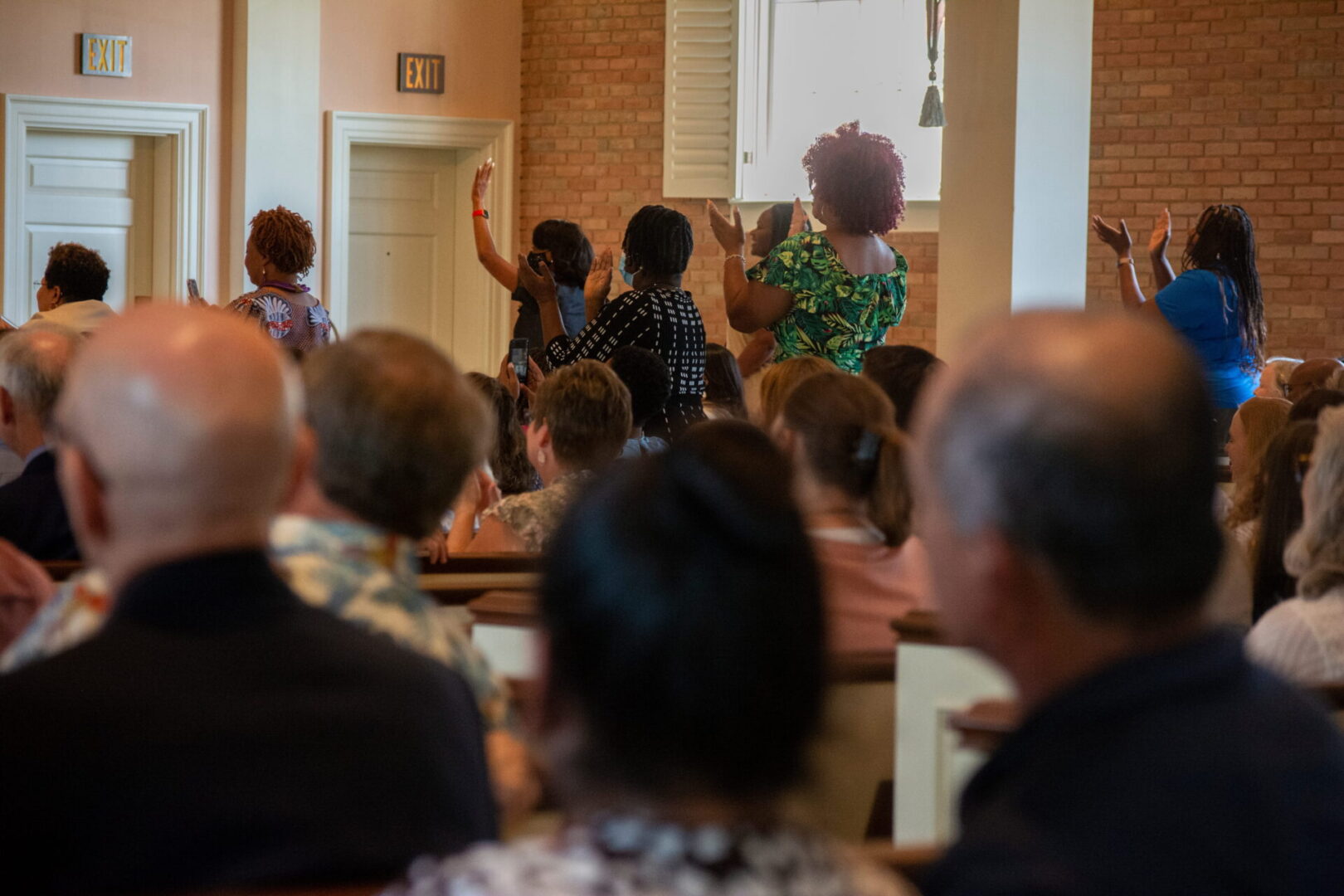 A group of people seated in a room, with some standing and raising their hands.
