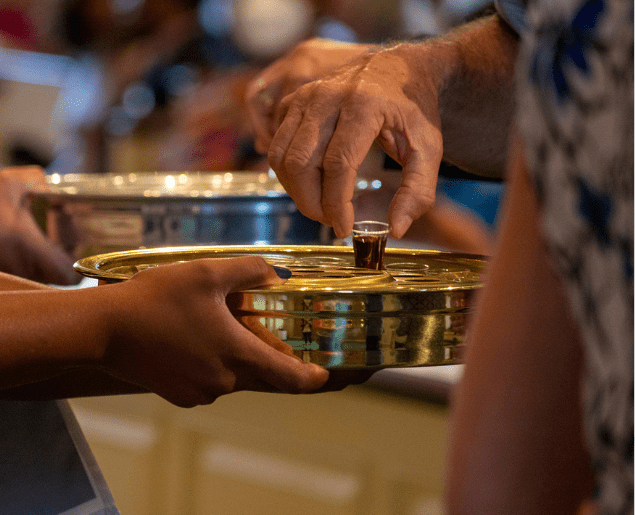 A person is being handed a small cup from a brass tray during a religious gathering.