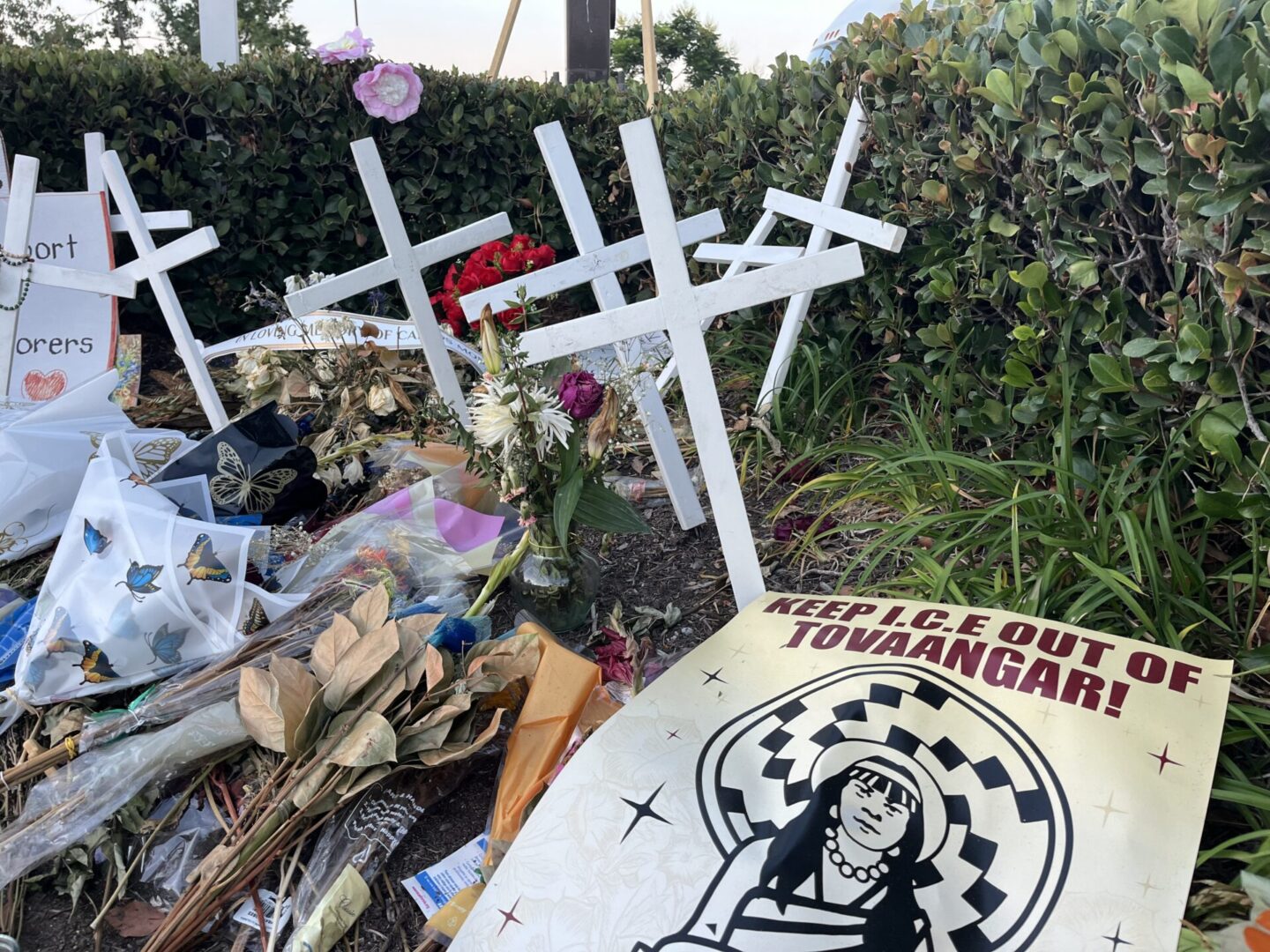 A memorial site with crosses, flowers, and a sign featuring an illustration and the words "Peace Out Toheganon."