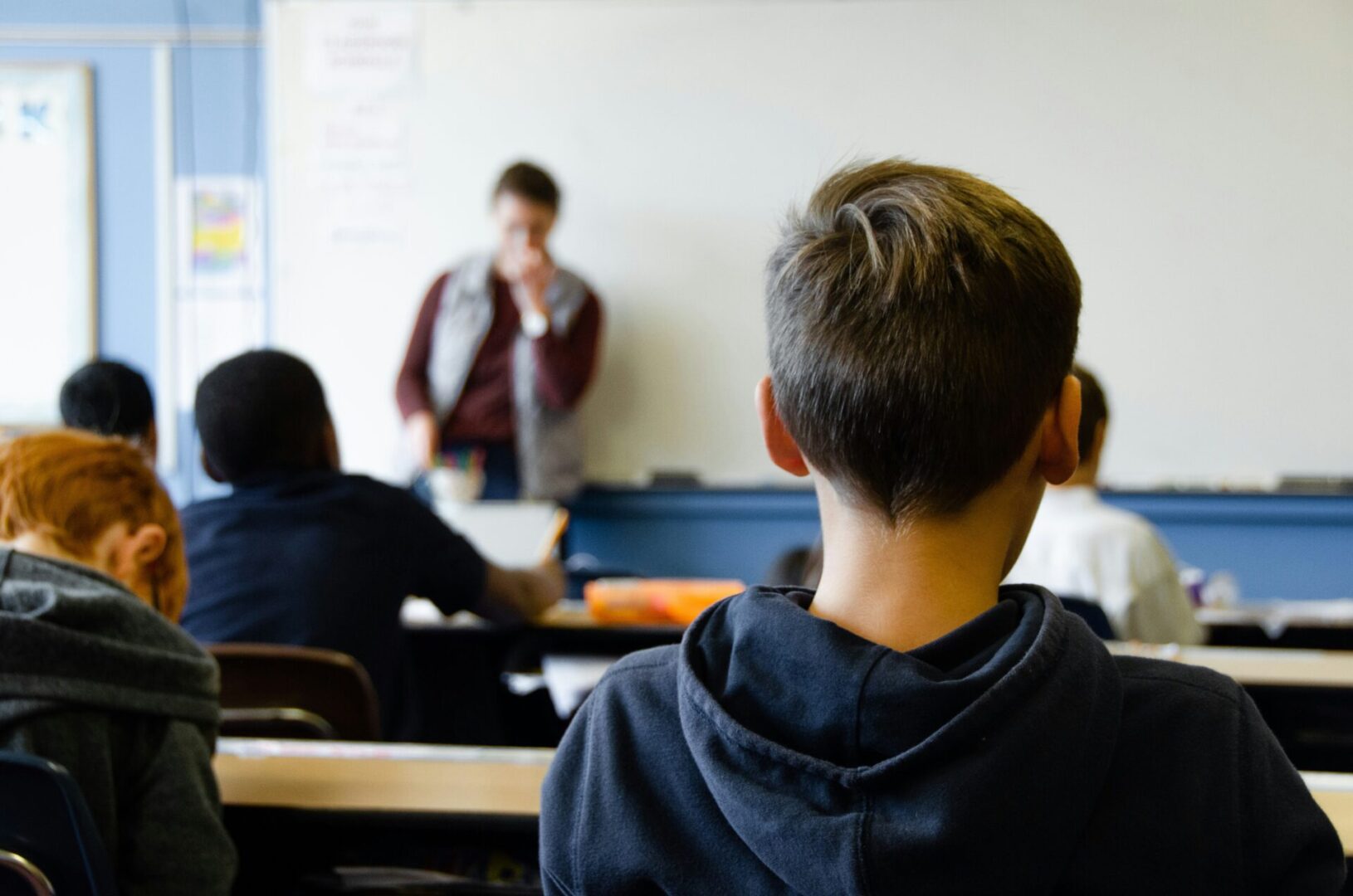 A classroom with students sitting at desks facing a teacher near a whiteboard.