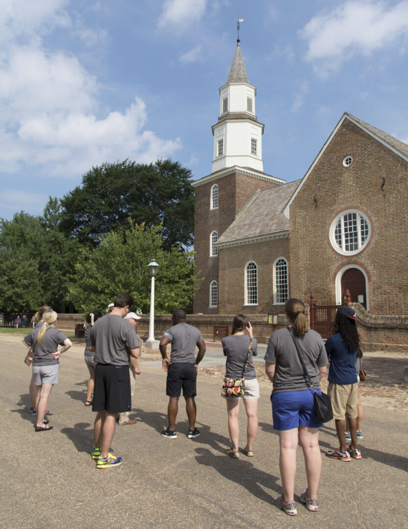 A group of people stand outside a historic church under a blue sky with scattered clouds.