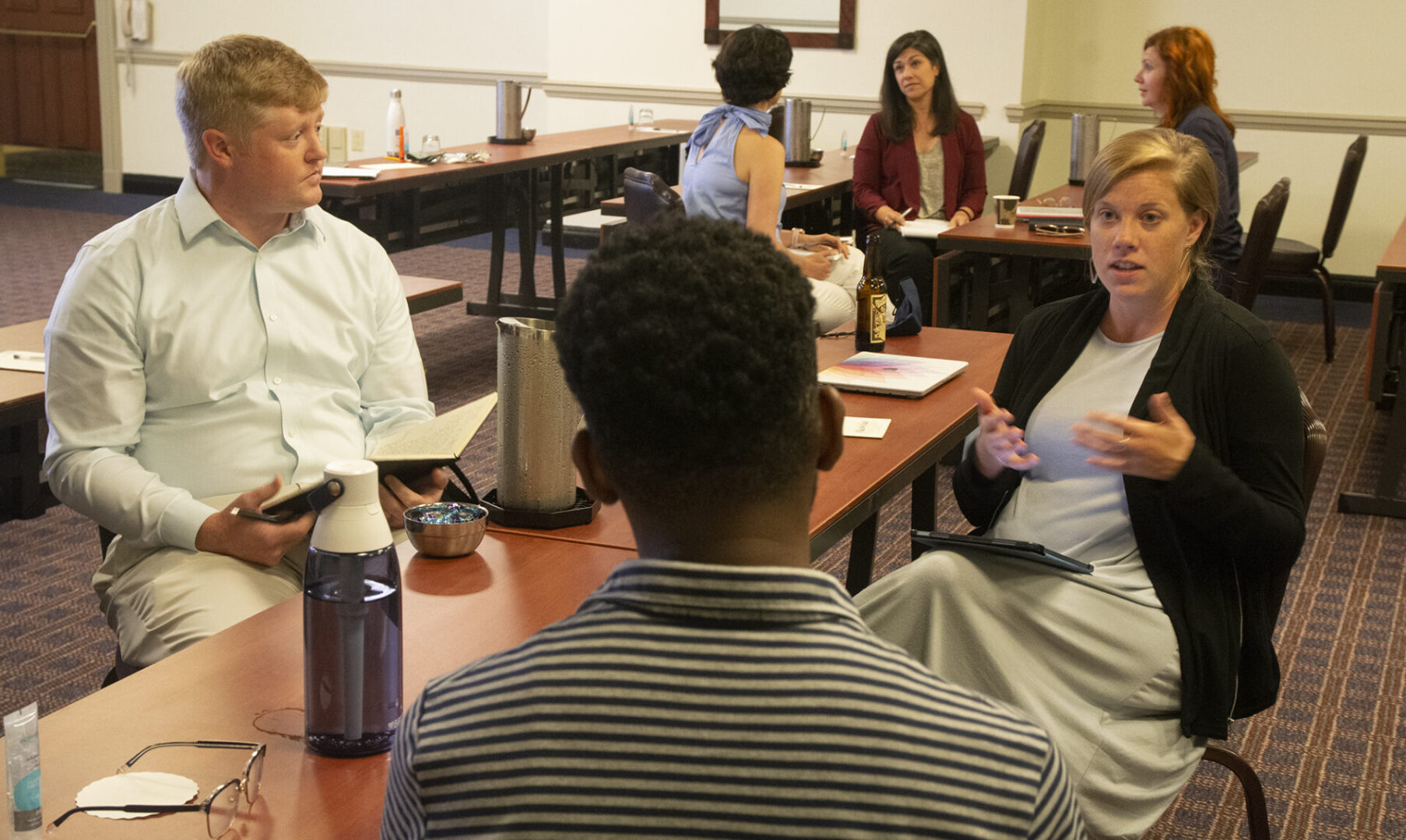 A group of people are engaged in a conversation around a table in a meeting room setting.