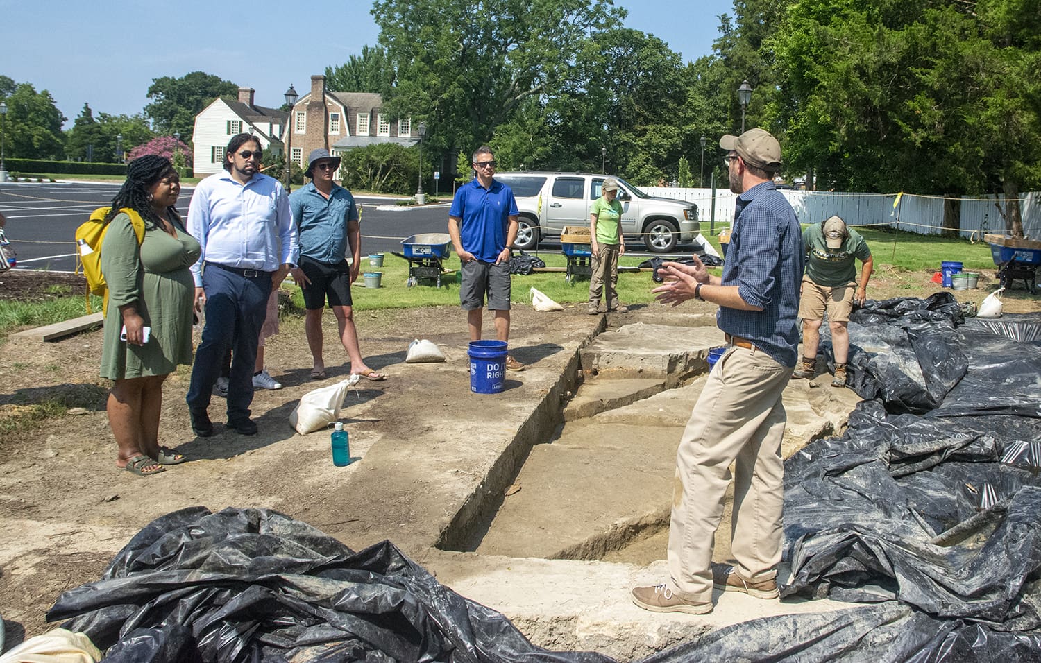 Archaeologists stand and discuss their work at an excavation site in an urban area.