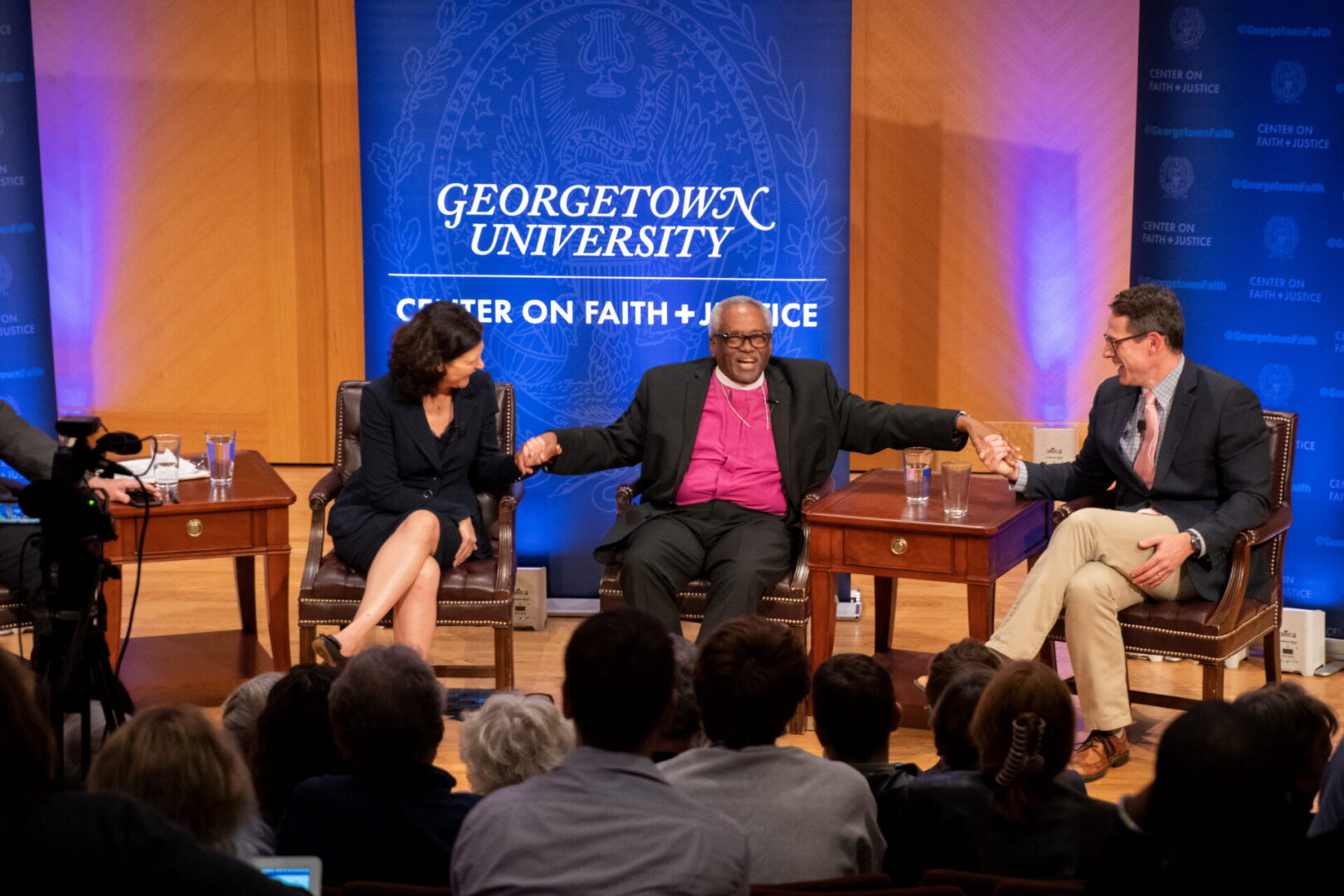 A discussion panel takes place at Georgetown University, featuring participants seated on stage in front of an audience.