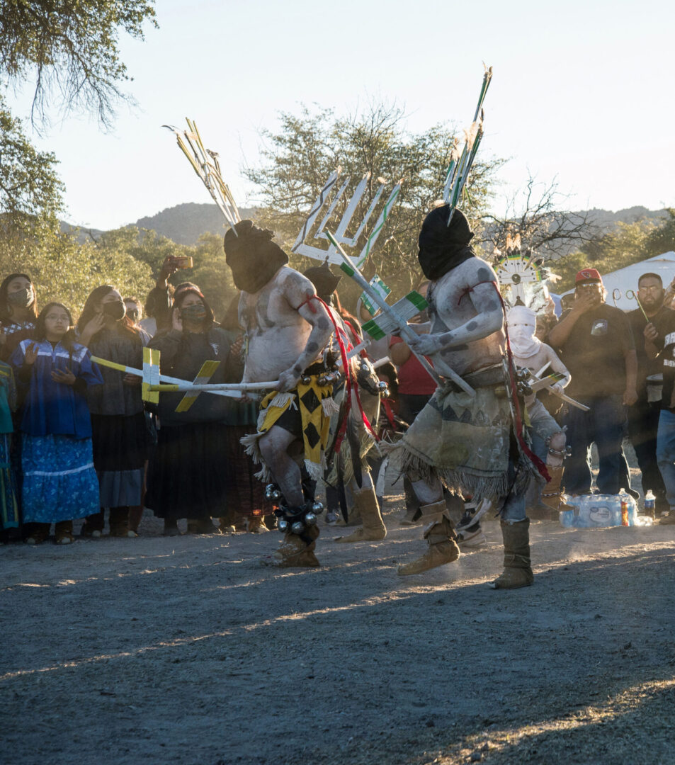 Dancers in traditional attire perform energetically in an outdoor setting surrounded by onlookers.