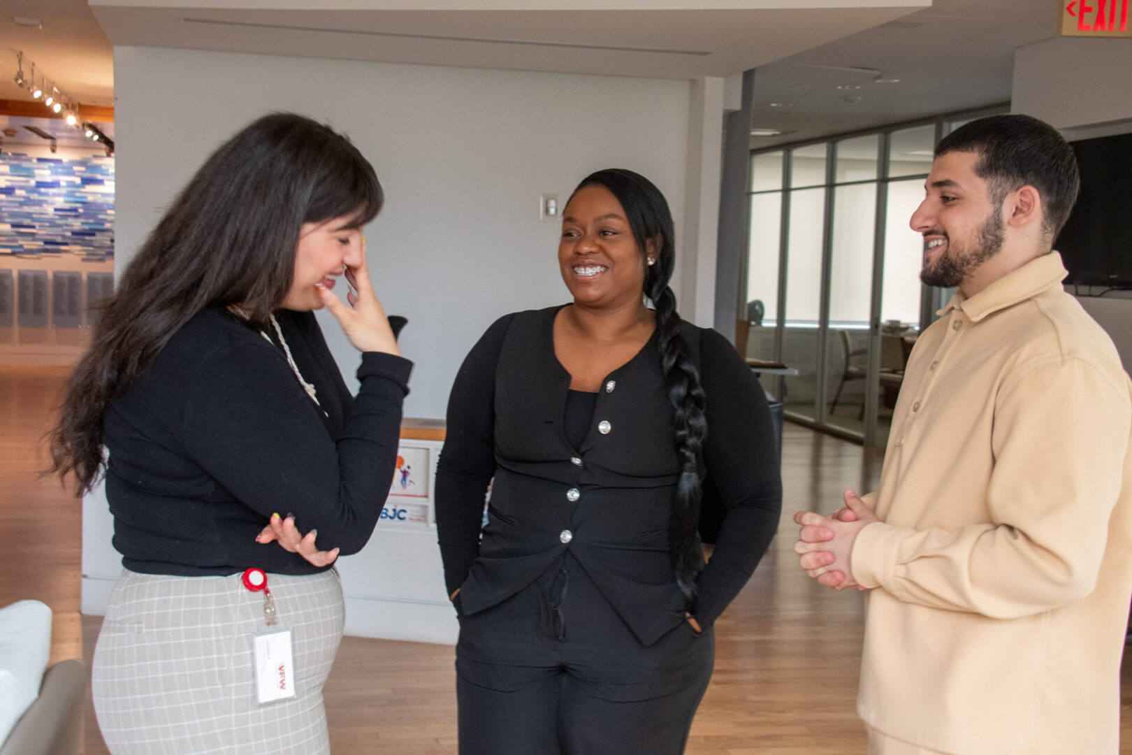 Three people are engaged in a friendly conversation in an office setting.