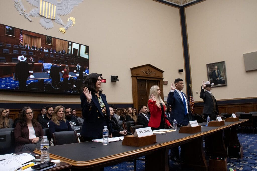 Individuals are standing in a formal setting, likely a hearing or meeting room, with some raising their right hands.