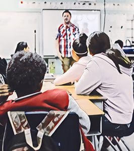 A teacher in a plaid shirt is standing in front of a classroom, engaging with students seated at desks.