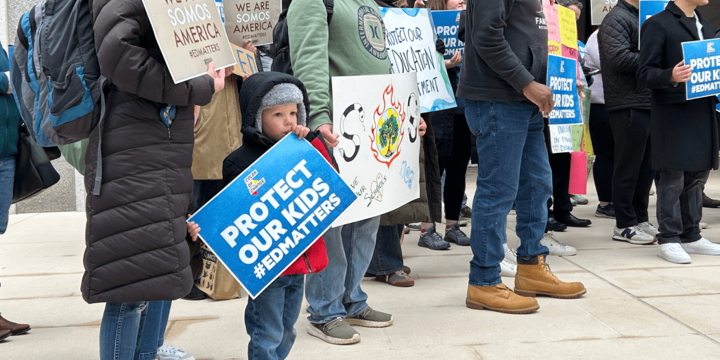 A group of people hold signs advocating for children's education and safety.