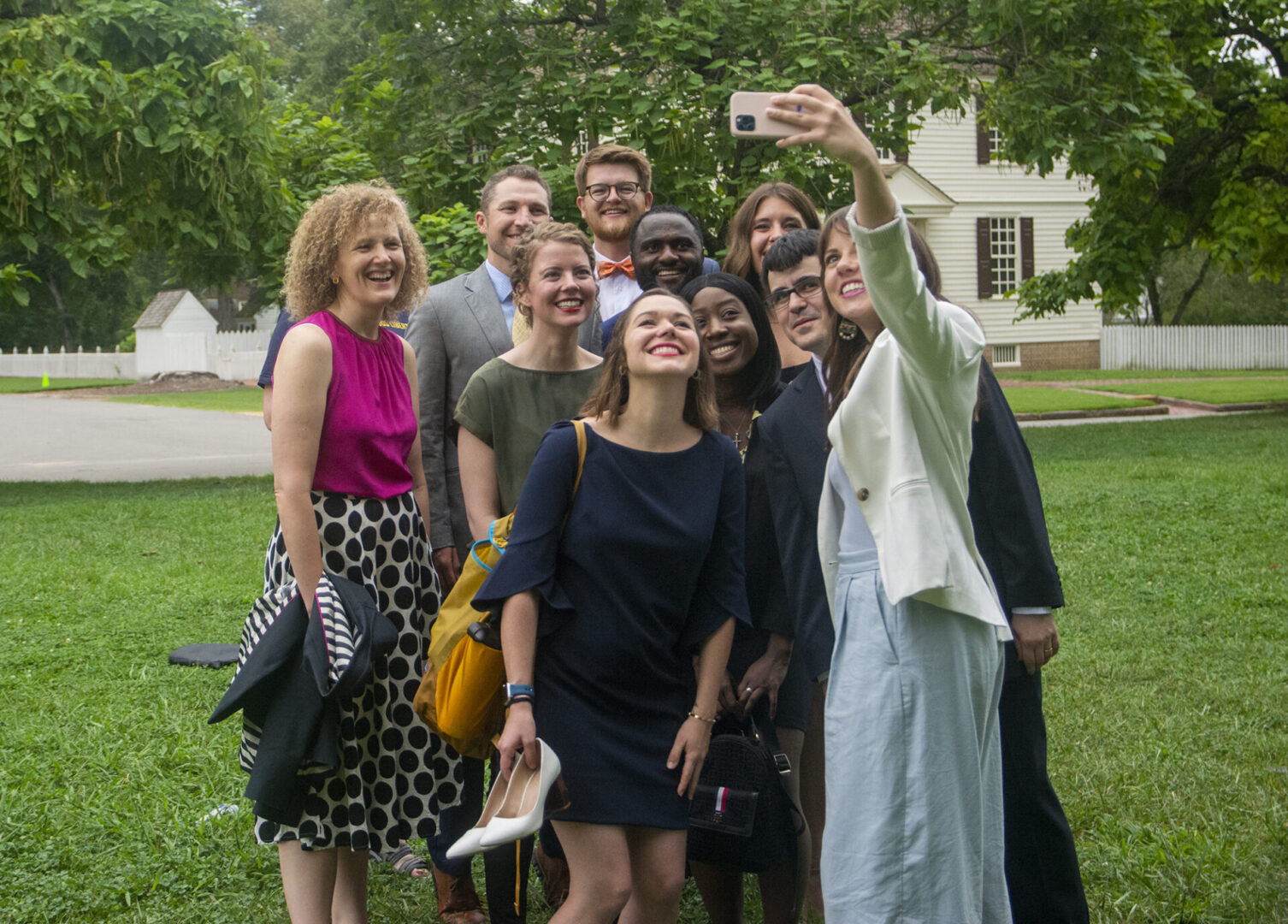 A group of people happily pose together outdoors as one of them takes a selfie.