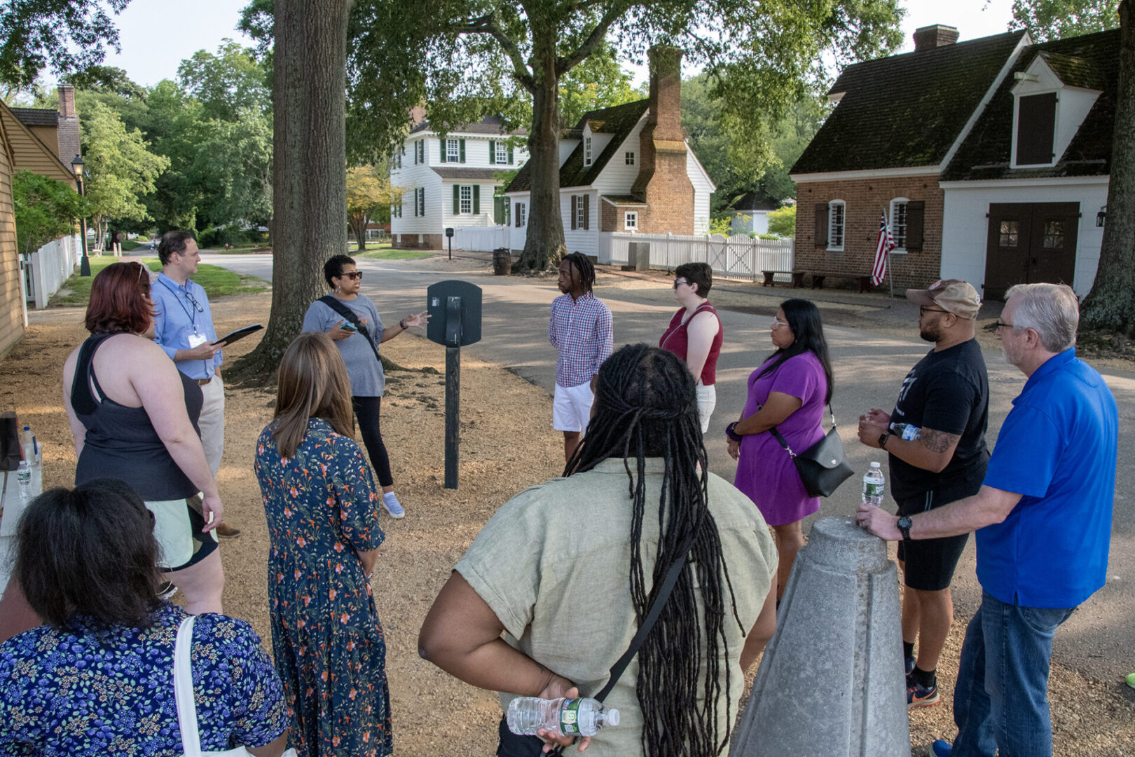 A group of people stands outdoors near a historical marker, listening to a guide.